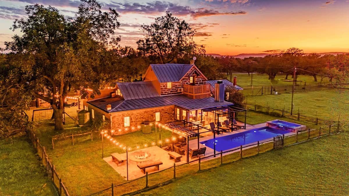 Hill Country stone estate with pool and string lights at dusk